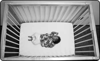 Small baby laying in a crib on their back without a blanket, toys, or pillows.