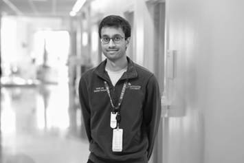 Rohith is wearing a dark quarter zip with the Nationwide Children's logo on it. He's standing in a hallway, smiling.